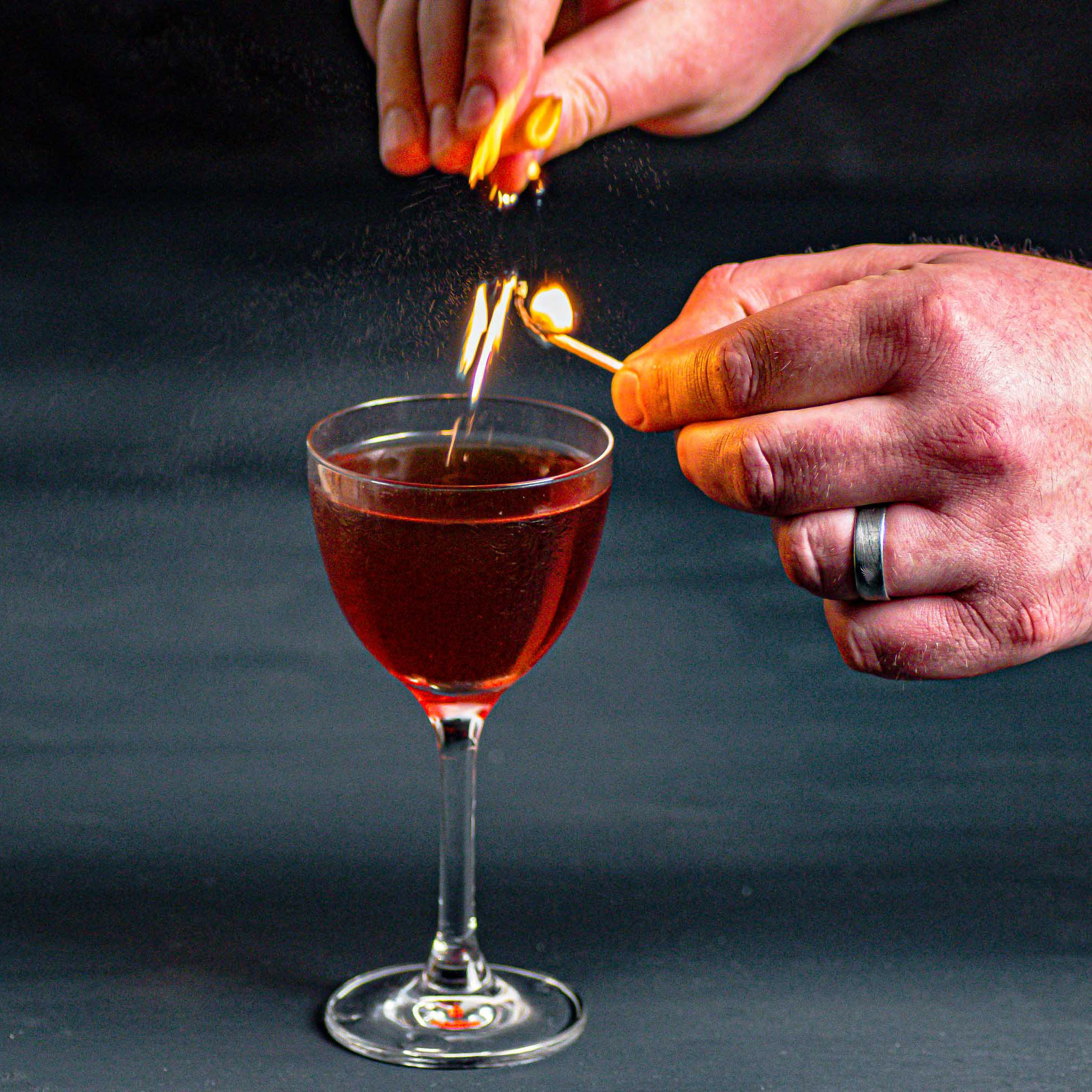 Ein Mancini Cocktail, der mit einer Orangenzeste abgeflämmt wird.
